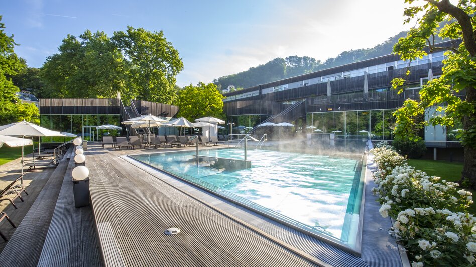 Modernes Thermal-Außenbecken in der Therme der Ruhe Bad Gleichenberg im Thermen- & Vulkanland Steiermark – stilvolle Wellnessoase mit Liegebereich, Sonnenschirmen und blühenden Rosen, umgeben von Natur und sanfter Hügellandschaft.