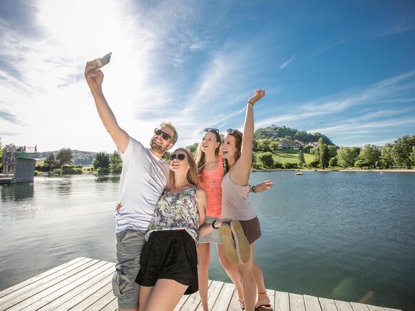 Familie macht Selfie vor Seebad mit Blick auf die Riegersburg