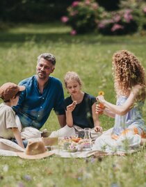 Eine Familie genießt das Picknick auf einer grünen Wiese im Thermen- & Vulkanland Steiermark