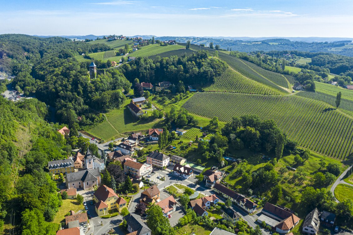 Luftaufnahme von Klöch mit Ortszentrum, Kirche und weitläufigen Weingärten in der hügeligen Landschaft des Thermen- & Vulkanlands Steiermark. | © Tourismusverband Thermen- & Vulkanland | pixelmaker.at