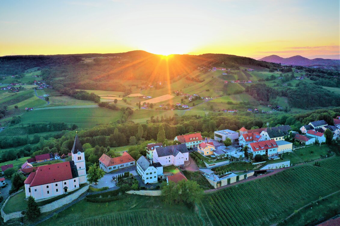 Sonnenuntergang über grünen Hügeln, steilen Weinhängen und der Kirche in St. Anna am Aigen im Thermen- & Vulkanland Steiermark