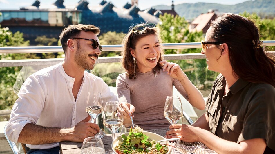 Freunde genießen regionale Kulinarik auf einer Terrasse am Schlossberg in Graz