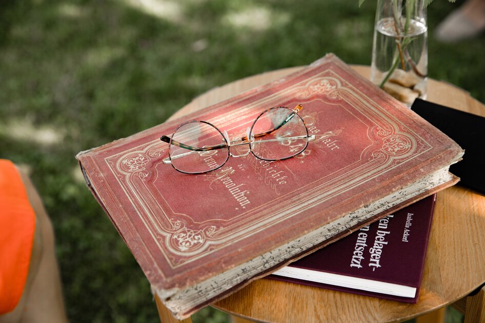 Kunst & Kulturin der Südsteiermark Buch mit rotem historischen Einband auf der eine runde goldene Lesebrille liegt.