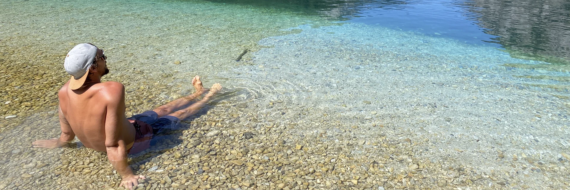 Entspannen am Leopoldsteinersee Ein Mann, der im seichten Wasser des klasklaren Leopoldsteinersee sitzt und auf die umliegende Bergkulisse blickt.