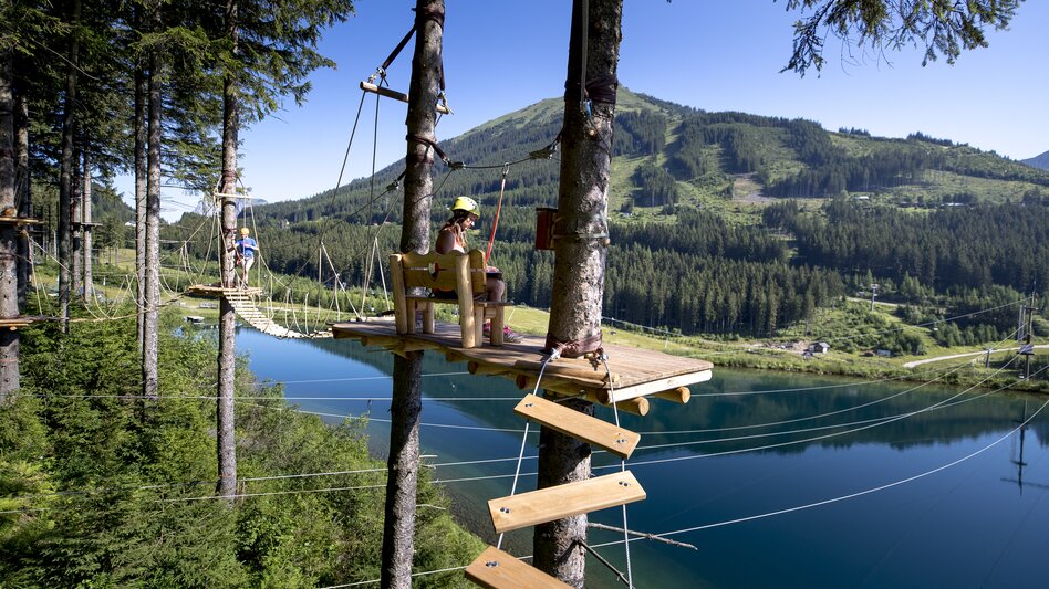 Kletterpark auf den Bäumen in der Höhe vor dem Grüblsee bei schönem Wetter.