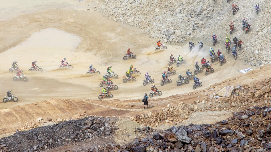 Viele Motorcrossfahrer fahren beim Erzberg Rodeo einen Hügel hinauf. Sie produzieren sehr viel Staub.