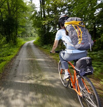 Eine Fahrradfahrerin mit großem Rucksack fährt durch den Wald