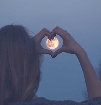 Eine Dame zeigt eine Hand in Herzform vor den Vollmond