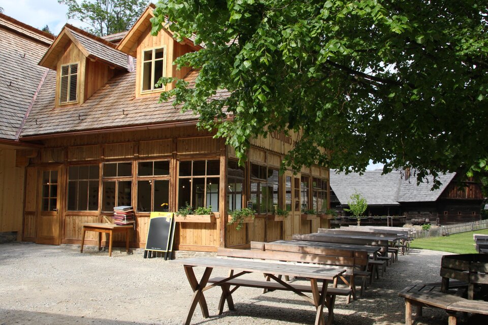 Holzgasthaus Zum Göller mit Gastgarten und Holzbänken im Freilichtmuseum Stübing in der Steiermark. | © Region Graz-Harry Schiffer