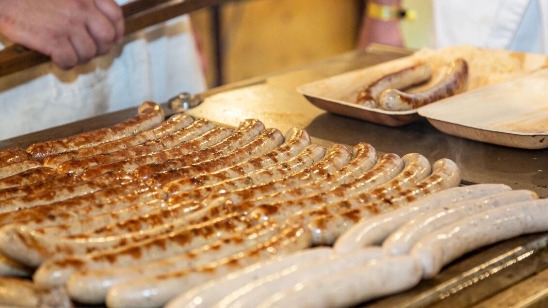 Gegrillte Würstchen auf einem Grill mit einer schönen Bräunung. Im Hintergrund sind die Hände eines Kochs zu sehen, der die Würstchen zubereitet. | © Freiwillige Feuerwehr Altaussee