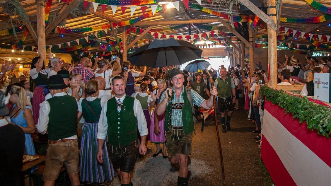 Eine lebhafte Feier in einer festlich dekorierten Halle mit vielen Menschen in traditioneller Tracht. Es gibt bunte Fahnen und festliche Stimmung. | © Freiwillige Feuerwehr Altaussee