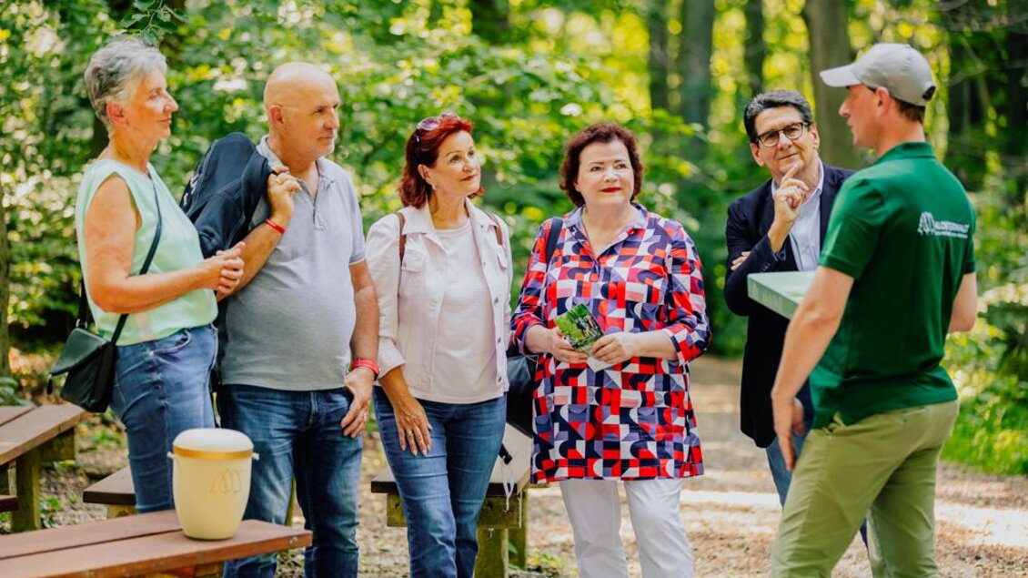 Eine Gruppe von sechs Personen steht im Wald und hört einem Guide zu. Es ist ein sonniger Tag, und die Umgebung ist grün und einladend. | © Klosterwald GmbH