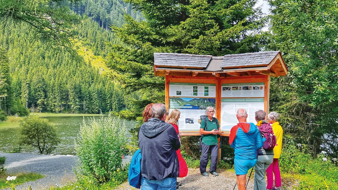 Eine Gruppe von Menschen diskutiert an einem Informationsstand in der Natur. Im Hintergrund sind Bäume und ein Gewässer sichtbar. | © Klosterwald GmbH