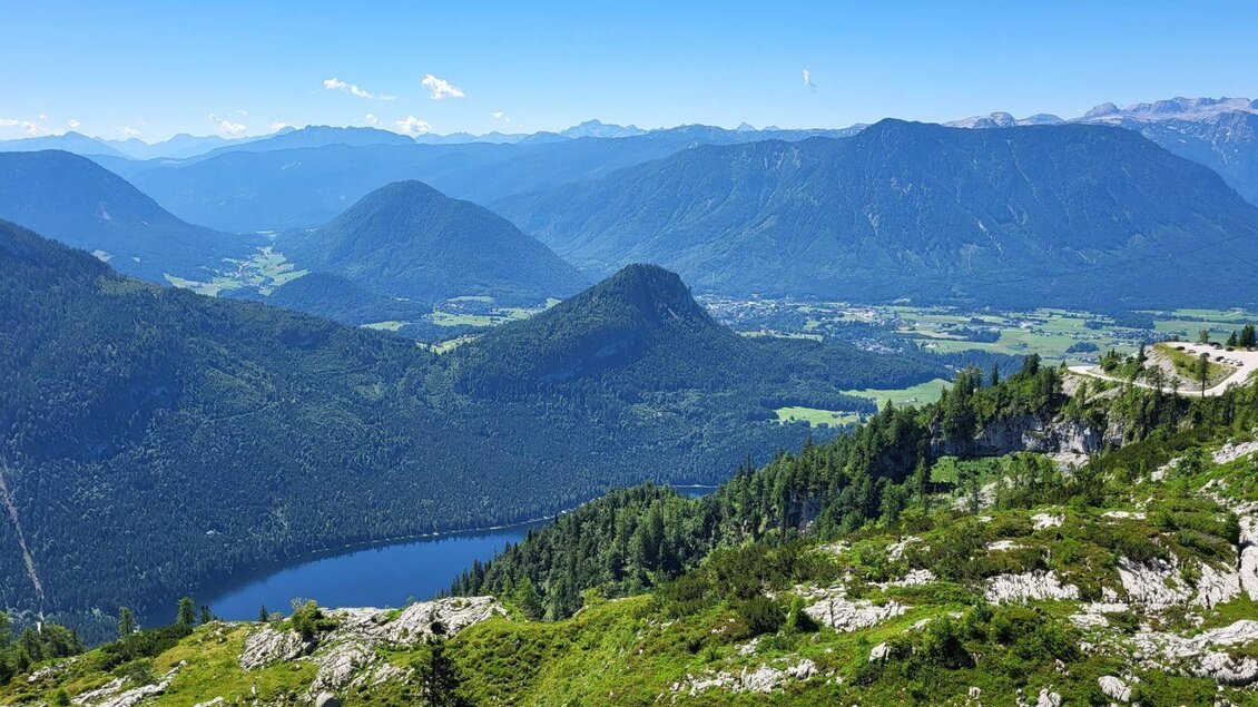 Eine beeindruckende Berglandschaft mit grünen Wiesen und einem blauen See. Im Hintergrund erstrecken sich majestätische Berge unter einem klaren Himmel. | © Petra Kirchschlager