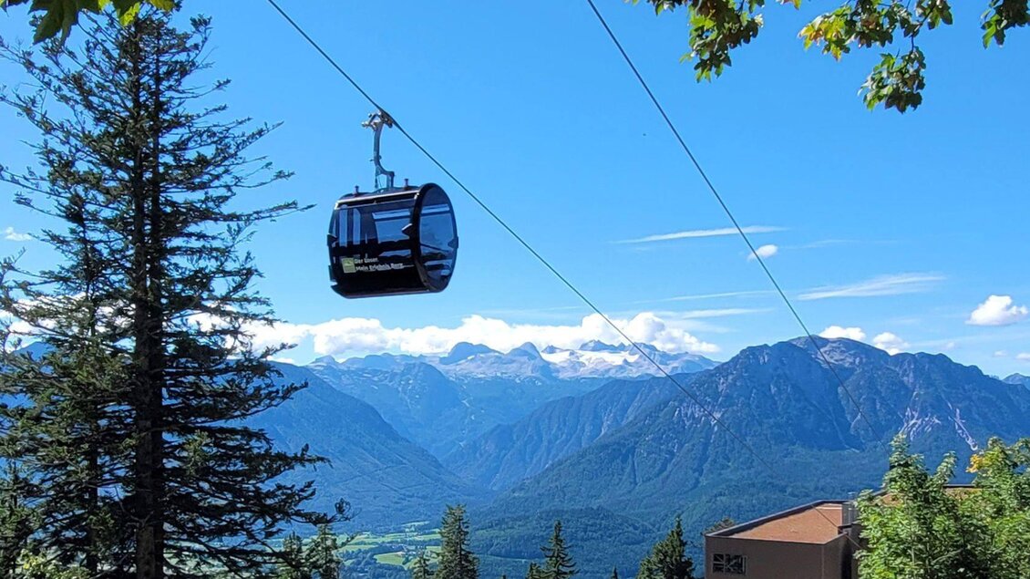 Eine Seilbahn schwebt über grüne Bäume und die Berge im Hintergrund. Der Himmel ist klar und blau, was eine malerische Landschaft entsteht. | © Rudolf Gasperl