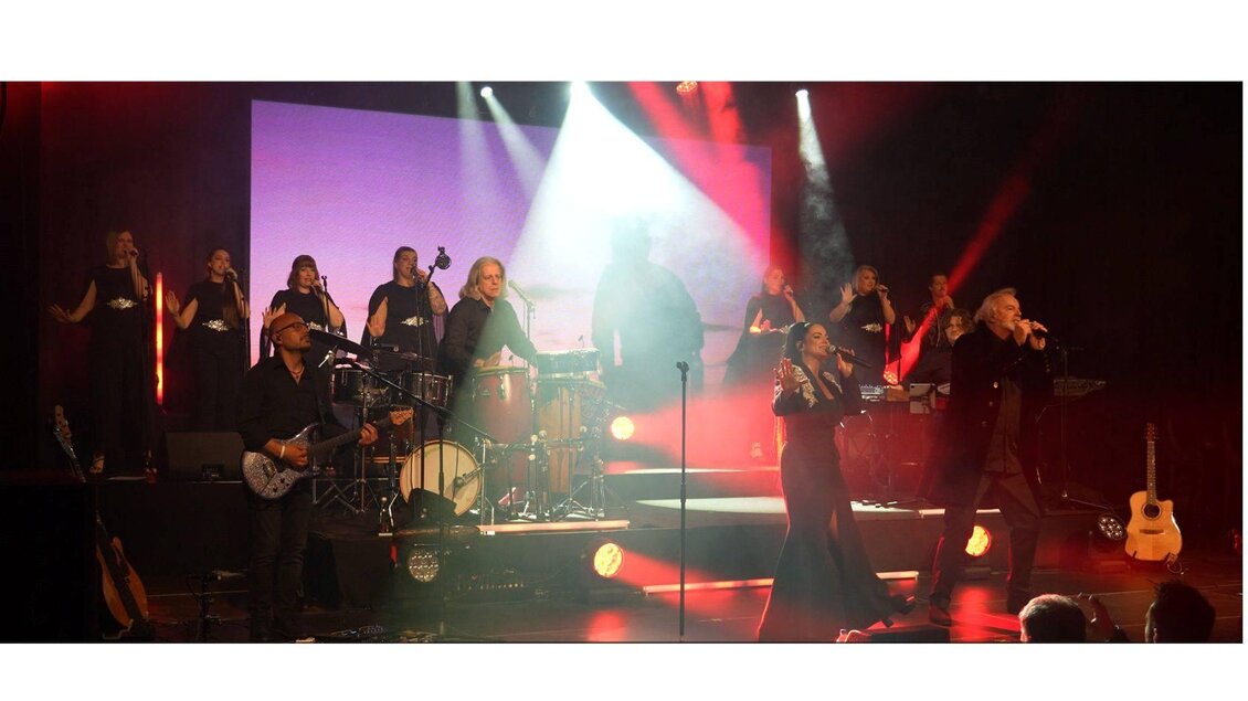 Eine live Musikaufführung mit mehreren Sängern und Musikern auf der Bühne. Die Atmosphäre ist dynamisch mit bunten Lichtern und einer engagierten Zuschauerschaft. | © Larissa Jaklitsch
