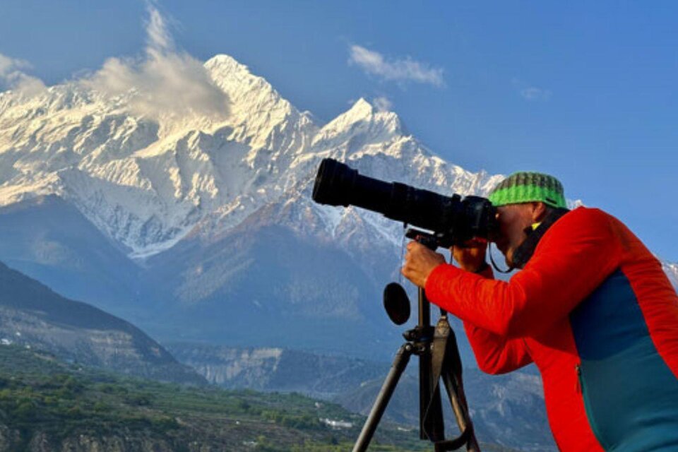 <p>Helmut Pichler steht inmitten der atemberaubenden Himalaya Landschaft mit seiner Kamera und einem Stativ und fotografiert die Natur.</p> | © Helmut Pichler