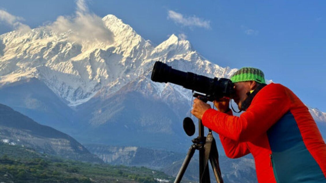 <p>Helmut Pichler steht inmitten der atemberaubenden Himalaya Landschaft mit seiner Kamera und einem Stativ und fotografiert die Natur.</p> | © Helmut Pichler