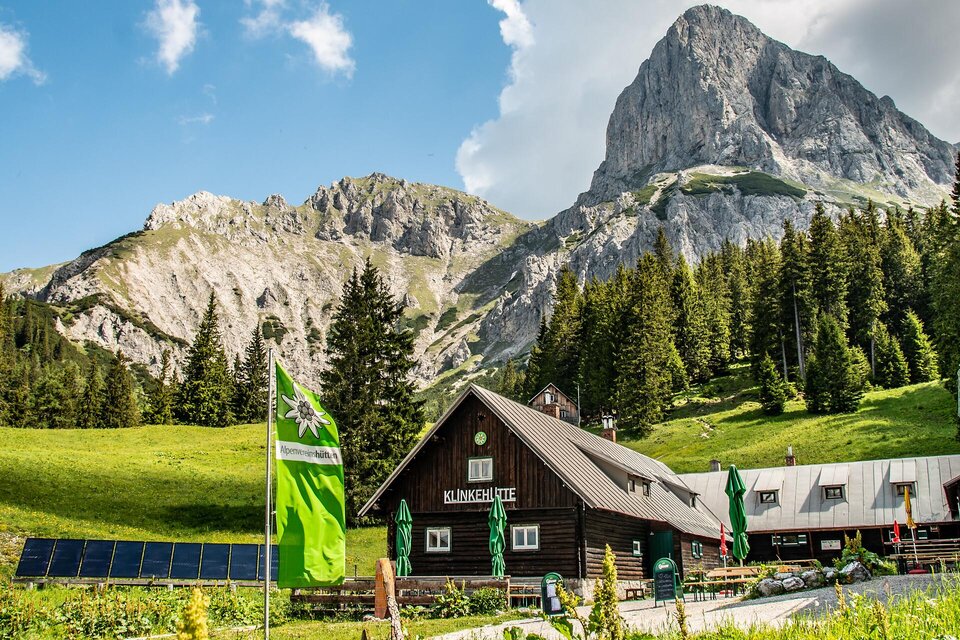 Eine malerische Berghütte umgeben von hohen Bergen und dichten Wäldern. Grüne Wiesen und sonniger Himmel sorgen für eine einladende Atmosphäre. | © TV Gesäuse