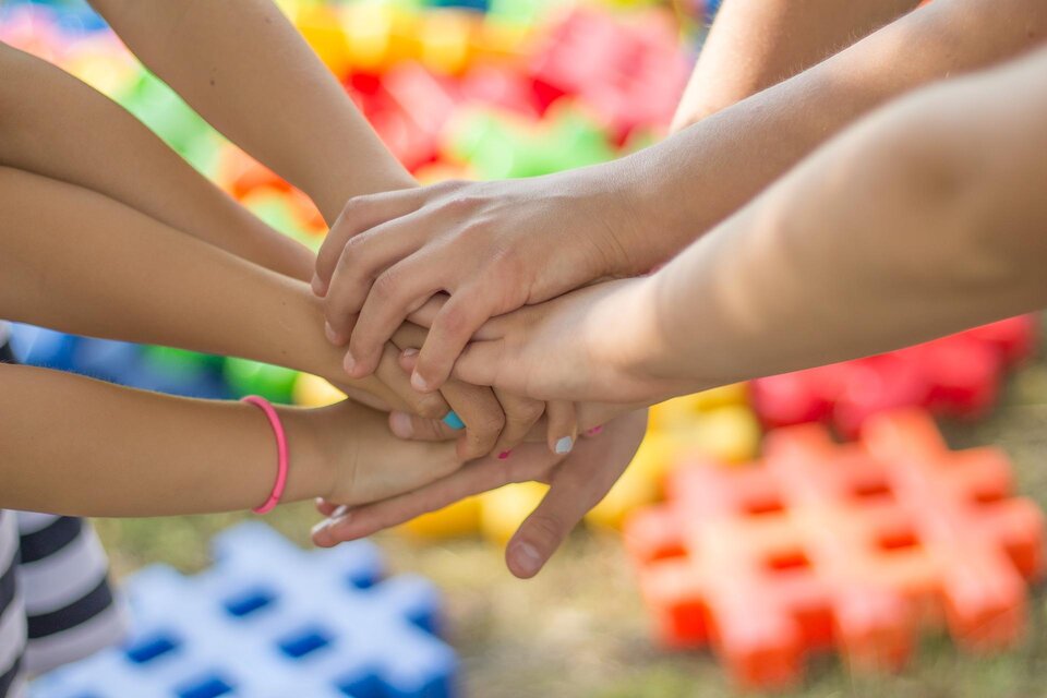 Eine Gruppe von Händen, die übereinander gelegt sind, symbolisiert Zusammenarbeit und Gemeinschaft. Im Hintergrund sind bunte Spielmatten sichtbar. | © Pixabay