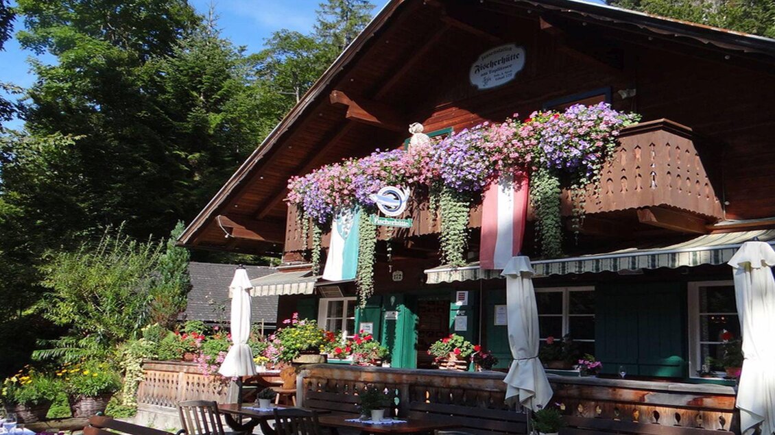 <p>Die charmante, rustikale Fischerhütte umgeben von Bäumen und bunten Blumen. Der Balkon ist mit Pflanzen dekoriert, und Tische stehen im Freien zum Verweilen mit Blick auf den Toplitzsee.</p>  | © Fischerhütte/Syen
