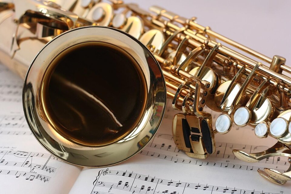 Ein glänzendes Saxophon liegt auf einem Notenblatt. Die Blätter zeigen musikalische Notationen und hinzufügen eine künstlerische Note zur Szene. | © Pixabay