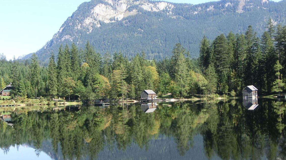 Ein See liegt mitten im Wald und am Ufer stehen vereinzelt kleine Bootshäuser und ein Badesteg führt ins Wasser.  | © Daniela Casari