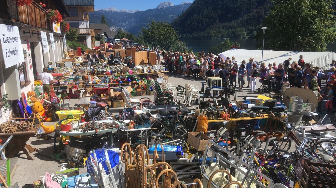 Ein Flohmarkt mit vielen verschiedenen Gegenständen und einer langen Schlange von Personen im Hintergrund. Die Umgebung ist von Bergen und einer schönen Landschaft umgeben. | © Freiwillige Feuerwehr Grundlsee