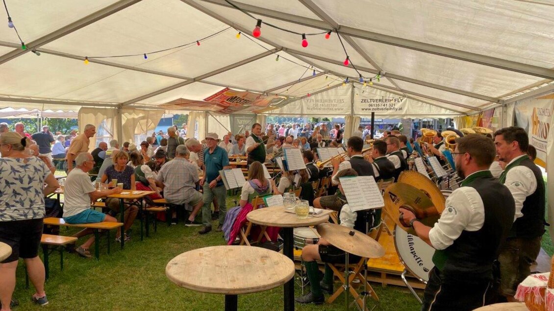 Eine lebhafte Musikkapelle spielt unter einem Zelt, während zahlreiche Gäste am Tisch sitzen. Die Atmosphäre ist festlich und gesellig. | © FF Grundlsee