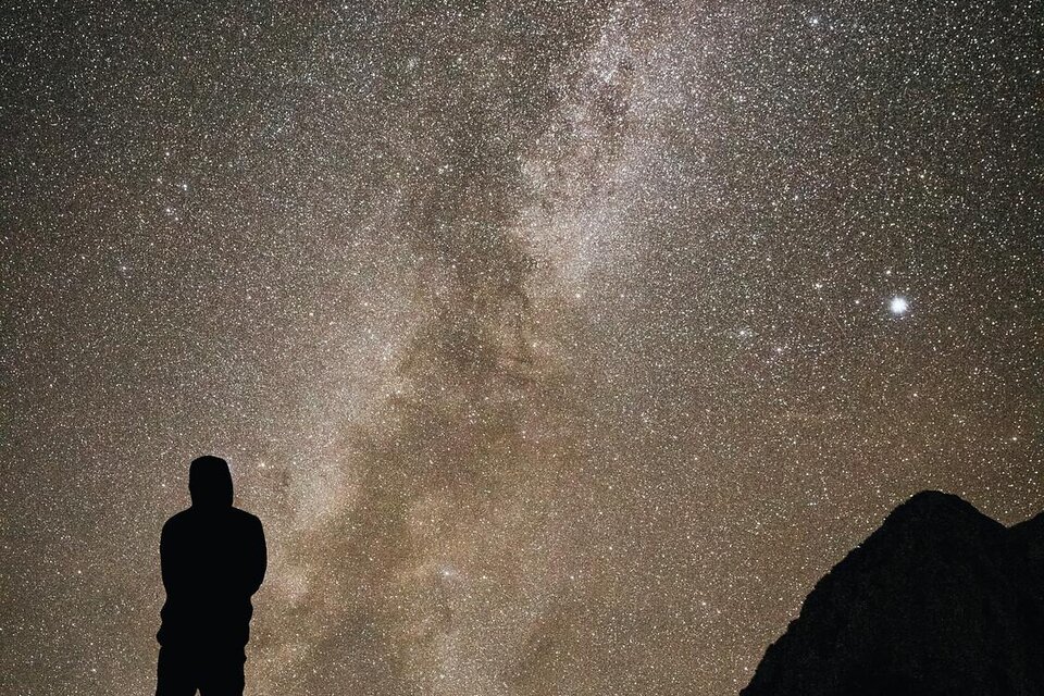 Eine Person steht auf einem Berg und blickt in den sternenklaren Nachthimmel. Die Milchstraße ist deutlich sichtbar. | © Stefan Leitner