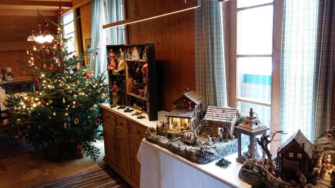 Ein festlich dekorierter Raum bei der Krippenausstellung auf der Blaa Alm. Neben dem beleuchteten Christbaum stehen die handgefertigte Krippen auf einem Tisch.  | © Petra Kirchschlager