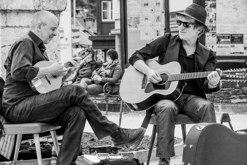 Zwei Musiker spielen auf einer Straße. Der eine spielt eine Mandoline, der andere eine Gitarre, während Passanten im Hintergrund zuschauen. | © Franz Thallhammer
