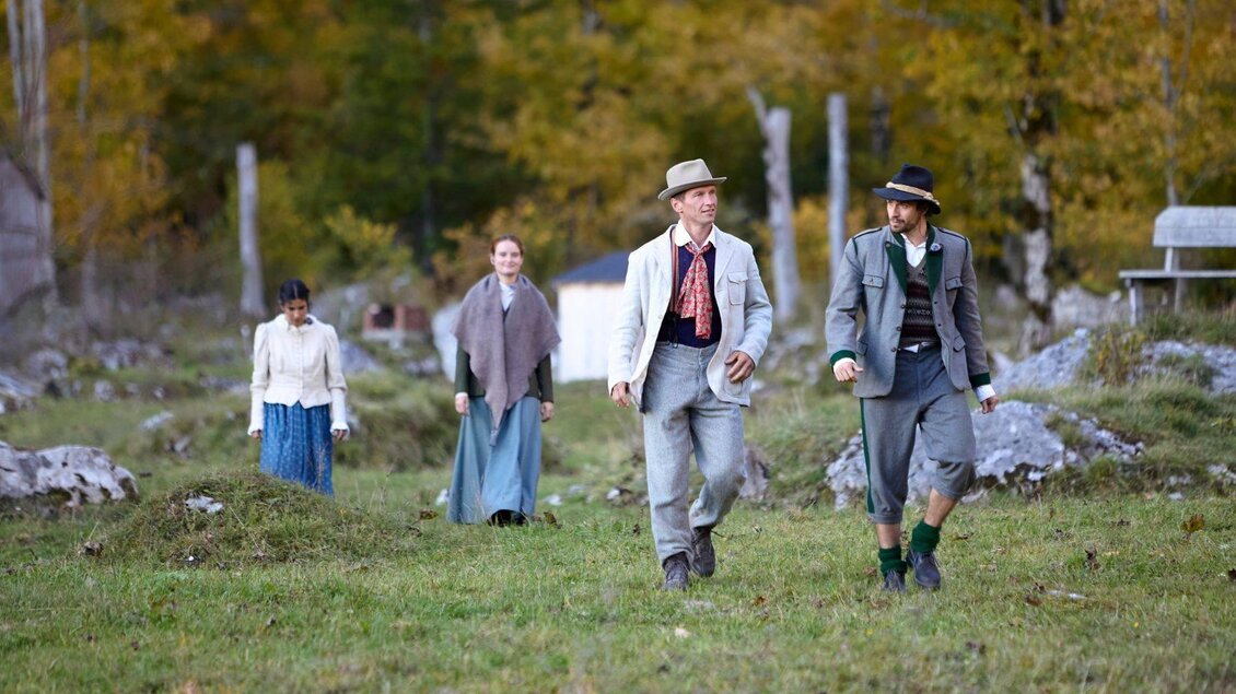 Vier Personen in historischer Kleidung gehen über eine grüne Wiese. Im Hintergrund sind Bäume und eine ländliche Kulisse zu sehen. | © Tauroa