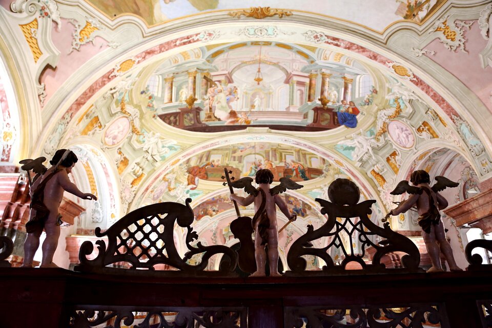 Eine kunstvoll verzierte Decke mit barocken Fresken. Im Vordergrund stehen zwei Engelstatuen, die den Blick auf die Malerei lenken. | © Stift Rein