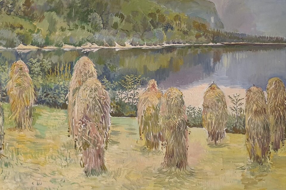Eine friedliche Landschaft mit einem See und überhängenden Bäumen im Hintergrund. Im Vordergrund stehen Strohfiguren auf einer Wiese. | © A. Schoiswohl