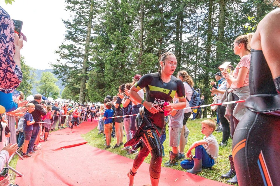 Eine Triathletin läuft auf einem roten Teppich vorbei, während Zuschauer sie anfeuern. Im Hintergrund sind Bäume und viele Menschen zu sehen. | © XTERRA