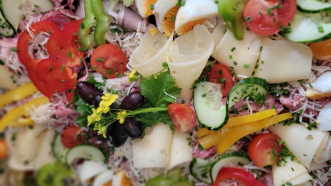 Ein bunter Salatarrangement mit frischem Gemüse und Käse. Es enthält Tomaten, Gurken, Paprika und Oliven. | © Hirschgehege Hauser