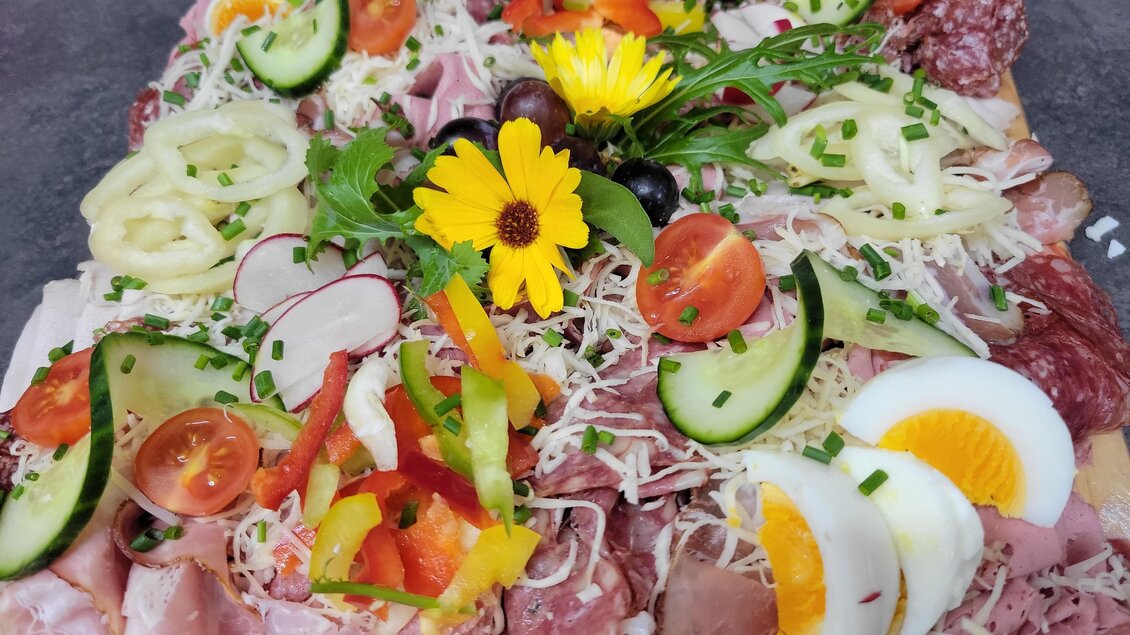 Ein bunt dekorierter Wurst- und Käseaufschnitt mit frischem Gemüse und einem Ei. Edle florale Akzente vervollständigen das ansprechende Arrangement. | © Hirschgehege Hauser