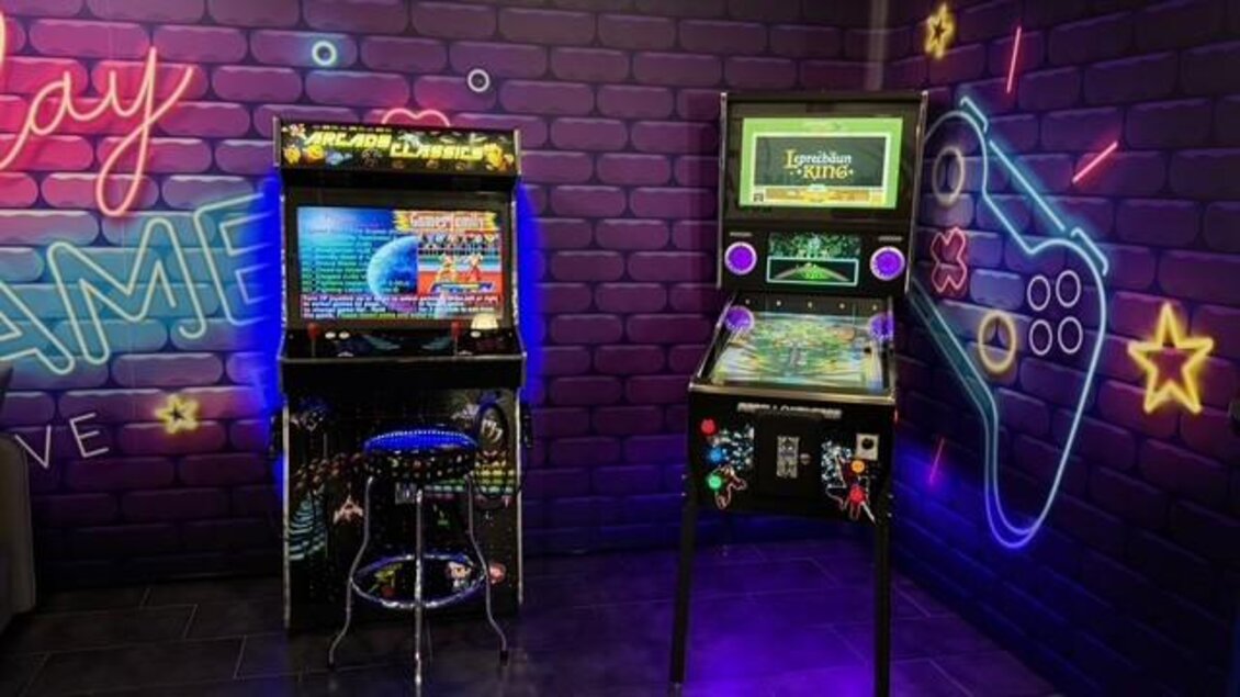 Ein moderner Spielbereich mit zwei Spielautomaten und einem Hocker. Die Wände sind kreativ mit bunten Neonlichtern decoriert. | © Thomas Zach