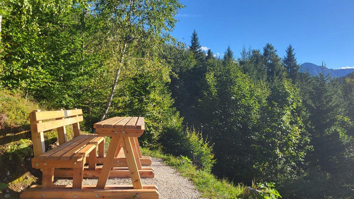 <p>Die Holzbank mit Tisch, auch als Bürgermeisterbankerl bekannt, steht auf einer Erhöhung, umgeben von dichten Bäumen. Im Hintergrund sind Berge unter einem klaren blauen Himmel zu sehen.</p> | © TVB Ausseerland Salzkammergut