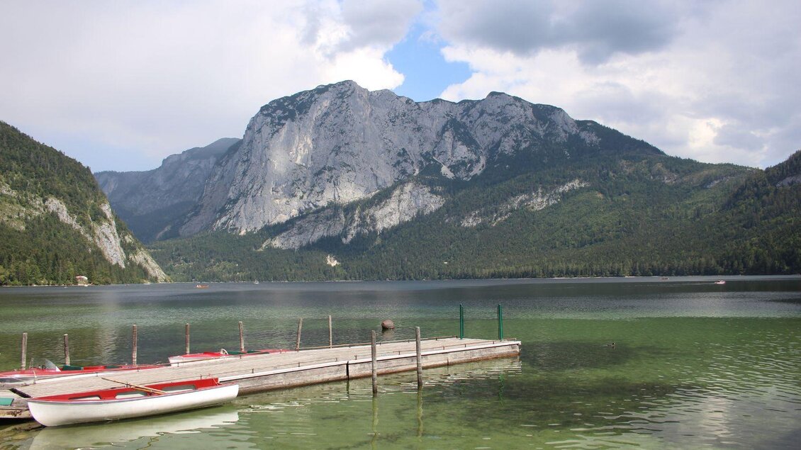Ein schöner Bergsee mit klarem Wasser und majestätischen Bergen im Hintergrund. Am Ufer liegen Boote auf einem Steg. | © Viola Lechner