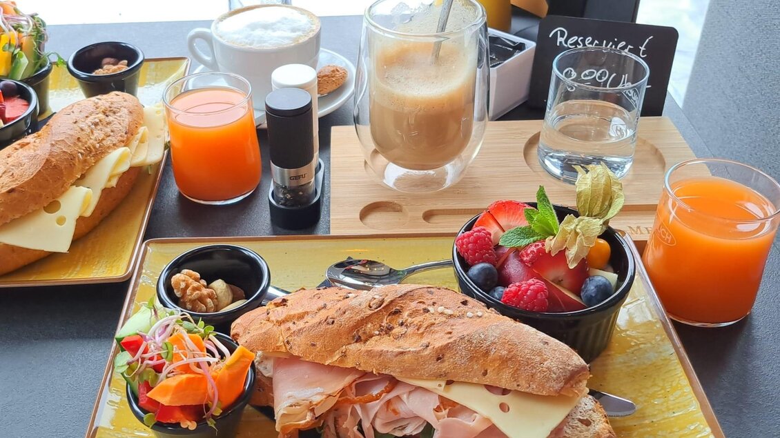 Ein schöner Frühstückstisch mit einem großen Sandwich, gefüllt mit Schinken und Käse. Dazu gibt es frisches Obst, Säfte und mehrere Getränke. | © Cafe Central