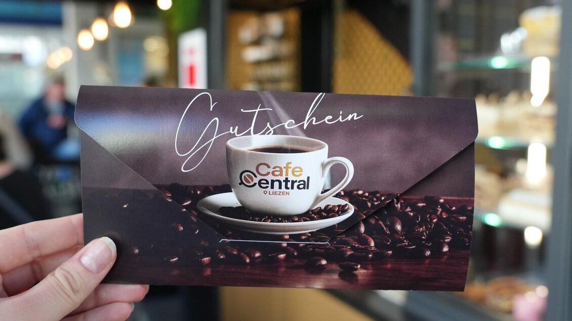 Ein Gutschein für das Café Central mit einer Tasse Kaffee und Kaffeebohnen im Hintergrund. Die Hand hält den Gutschein in einem modernen Café. | © Cafe Central