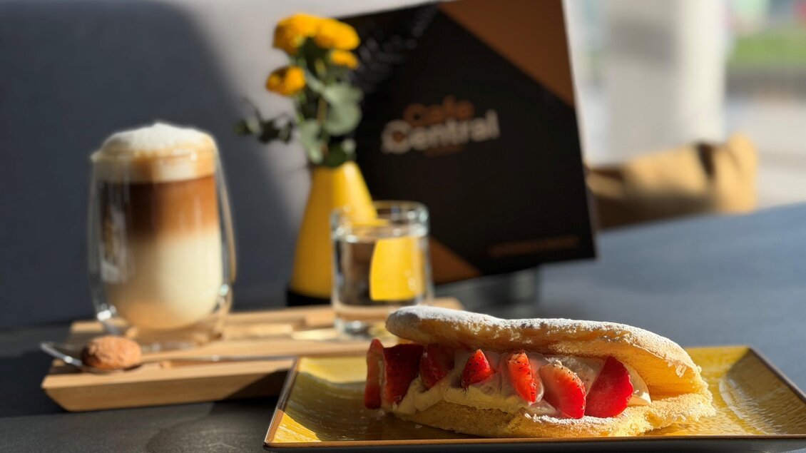 Ein leckerer Teller mit einem Dessert und frischen Erdbeeren, garniert mit Puderzucker. Dazu ein Glas Kaffee und eine kleine Blumenvase auf dem Tisch. | © Cafe Central
