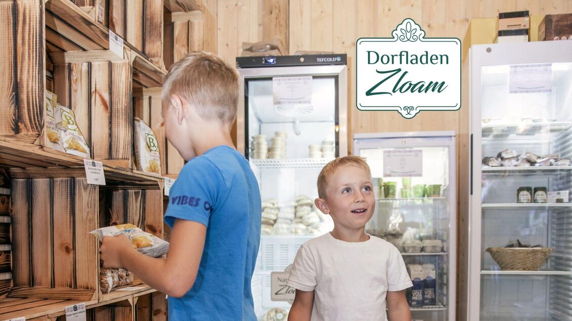 Ein schöner Dorfladen mit Regalen aus Holz und vielen Produkten. Zwei Kinder erkunden die Waren und haben Spaß dabei. | © www.zloam.at
