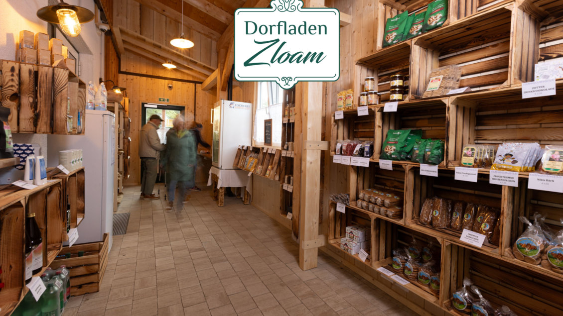 Ein gemütlicher Dorfladen mit Regalen aus Holz, gefüllt mit regionalen Produkten. Im Hintergrund sind Kunden beim Einkaufen zu sehen. | © Narzissendorf Zloam, www.zloam.at