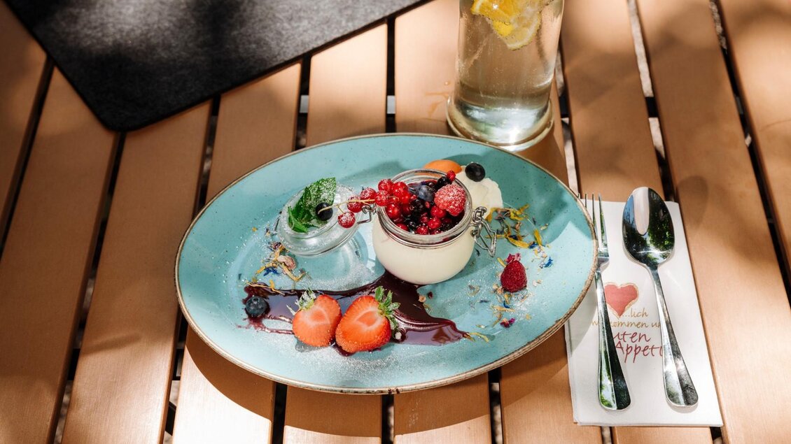 <p>Ein elegantes Dessert auf einem blauen Teller, garniert mit frischen Beeren und Minze. Daneben steht ein Erfrischungsgetränk.</p> | © Gasthaus Stöckl