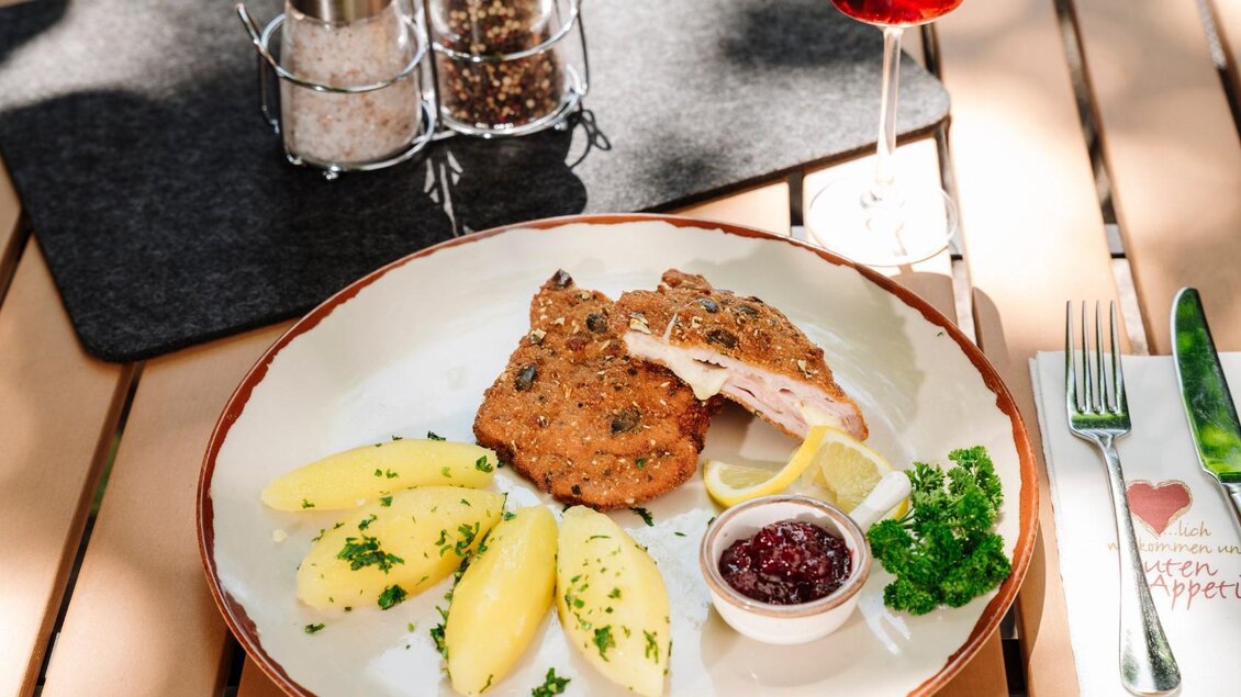 <p>Ein Teller mit einem panierten Schnitzel Cordon Bleu, Kartoffeln und Preiselbeersoße. Dazu ein Glas und Gewürzmühlen auf einem Tisch.</p> | © Gasthaus Stöckl