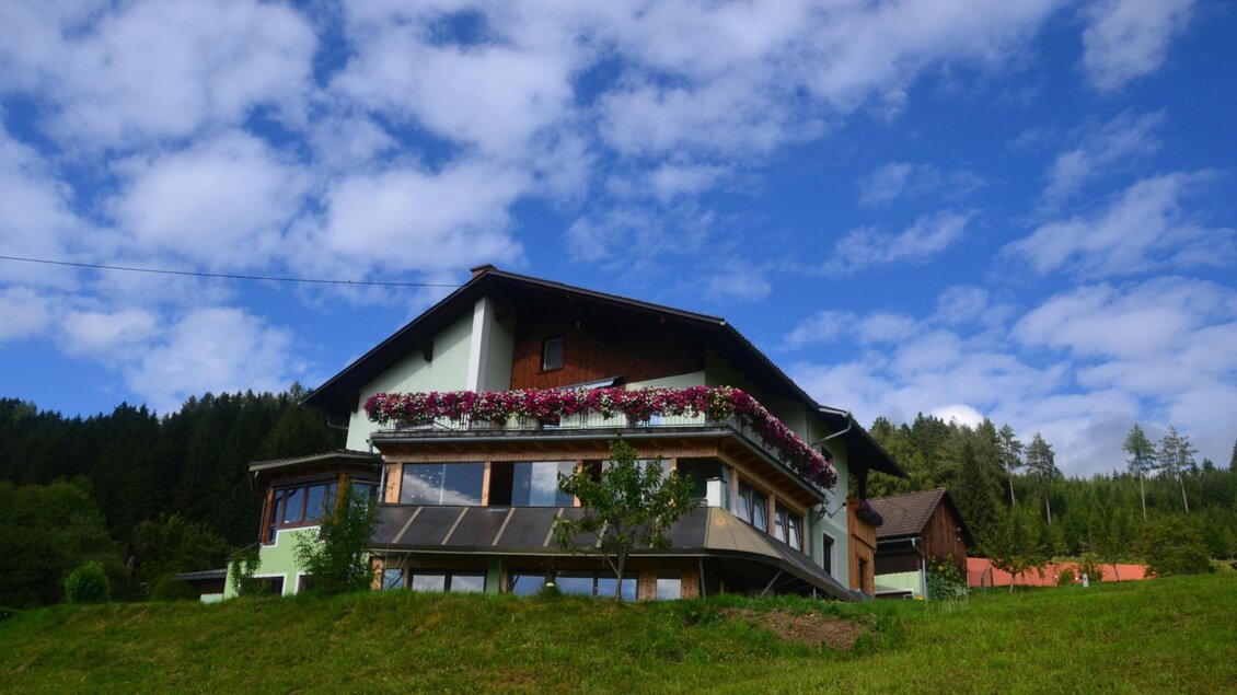 Ein schöner Bauernhof im Grünen mit blühenden Pflanzen und einem klaren blauen Himmel. Umgeben von Wäldern bietet er eine idyllische Aussicht. | © Moarbauerhof