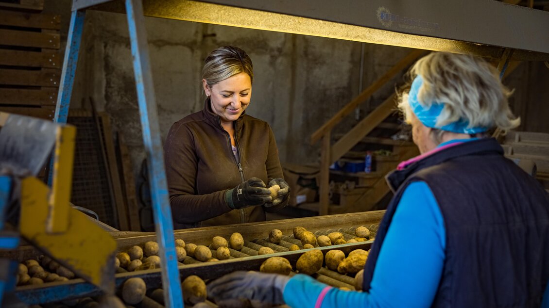 Zwei Frauen arbeiten an einem Tisch mit Kartoffeln. Eine Frau schält eine Kartoffel, während die andere aufmerksam zusieht. | © Netzwerk Kulinarik Wildbild